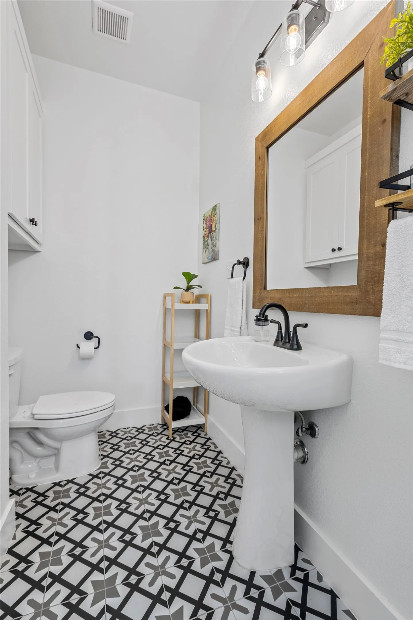 Pedestal sink with matte black faucet, patterned floor tiles, recessed wall cabinet, and a framed mirror (second on suite bathroom)