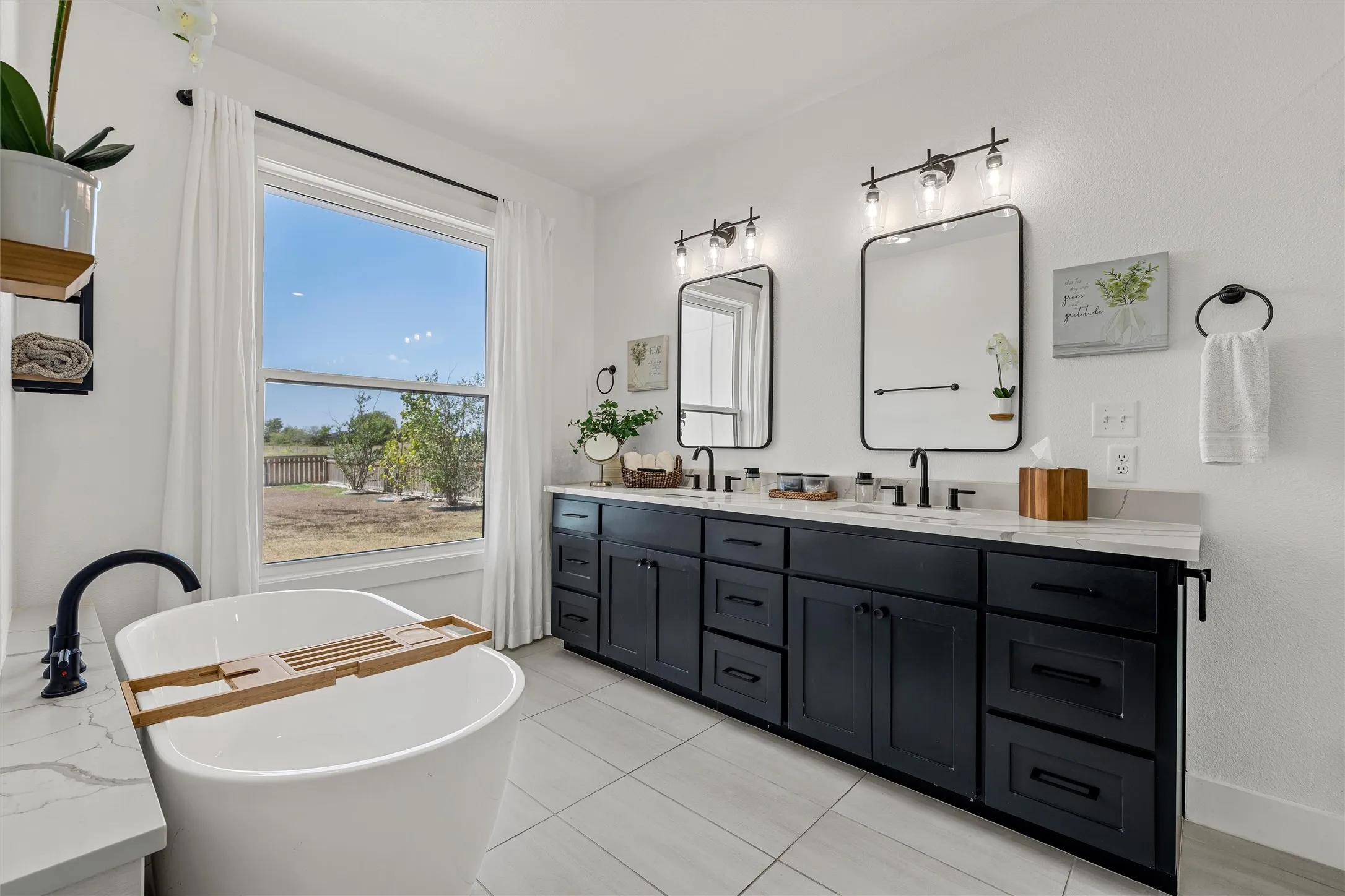 Bright bathroom featuring a freestanding tub with matte black fixtures, a dual vanity with a light-toned countertop, black cabinetry, and two rectangular mirrors