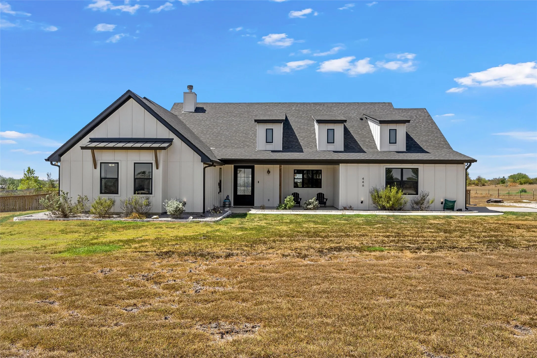Modern farmhouse exterior featuring white vertical siding, black-framed windows, a dark shingled roof, a prominent front gable, and three dormer windows