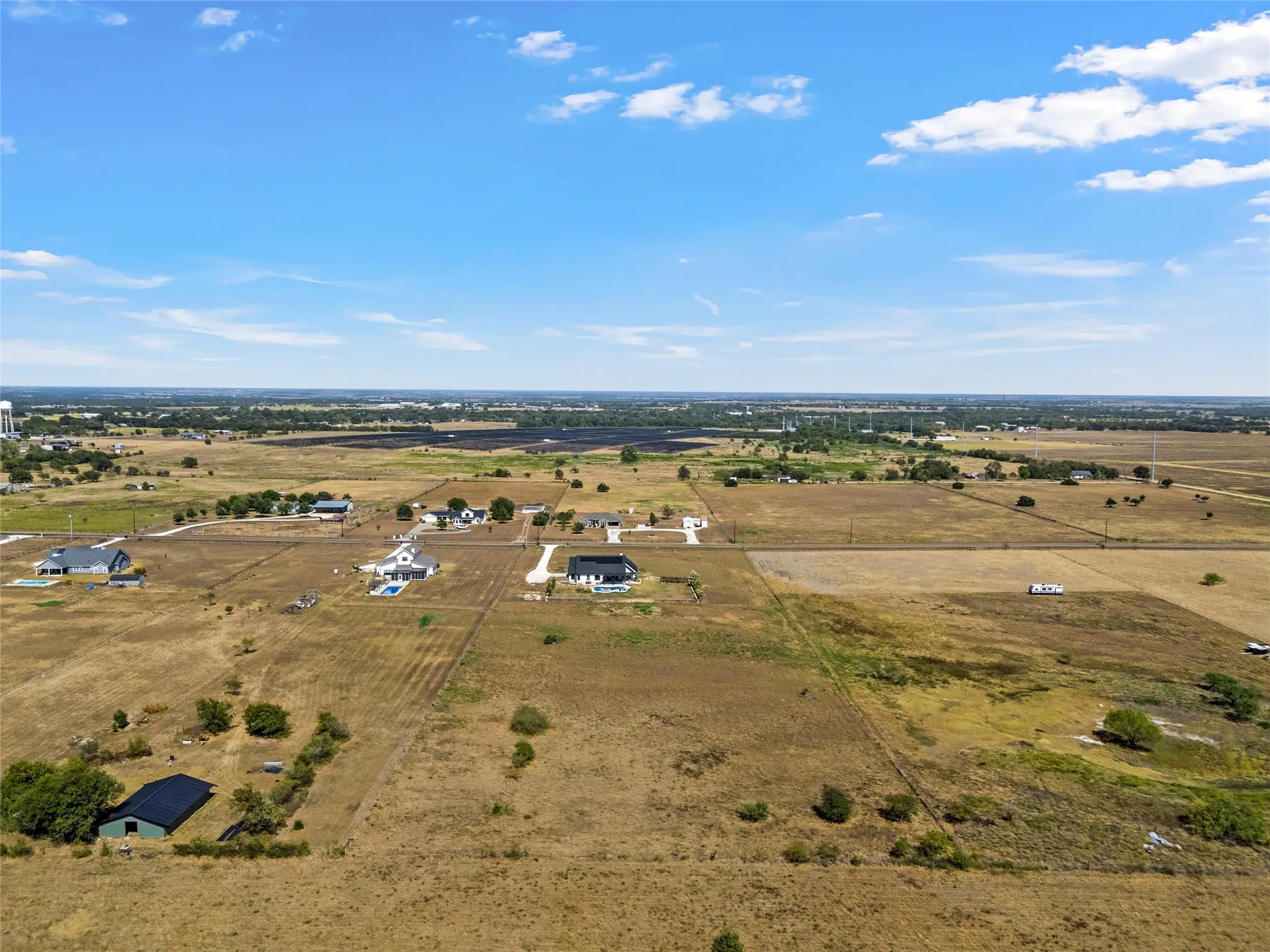Rural landscape featuring expansive undeveloped land, scattered residential structures, and distant agricultural fields