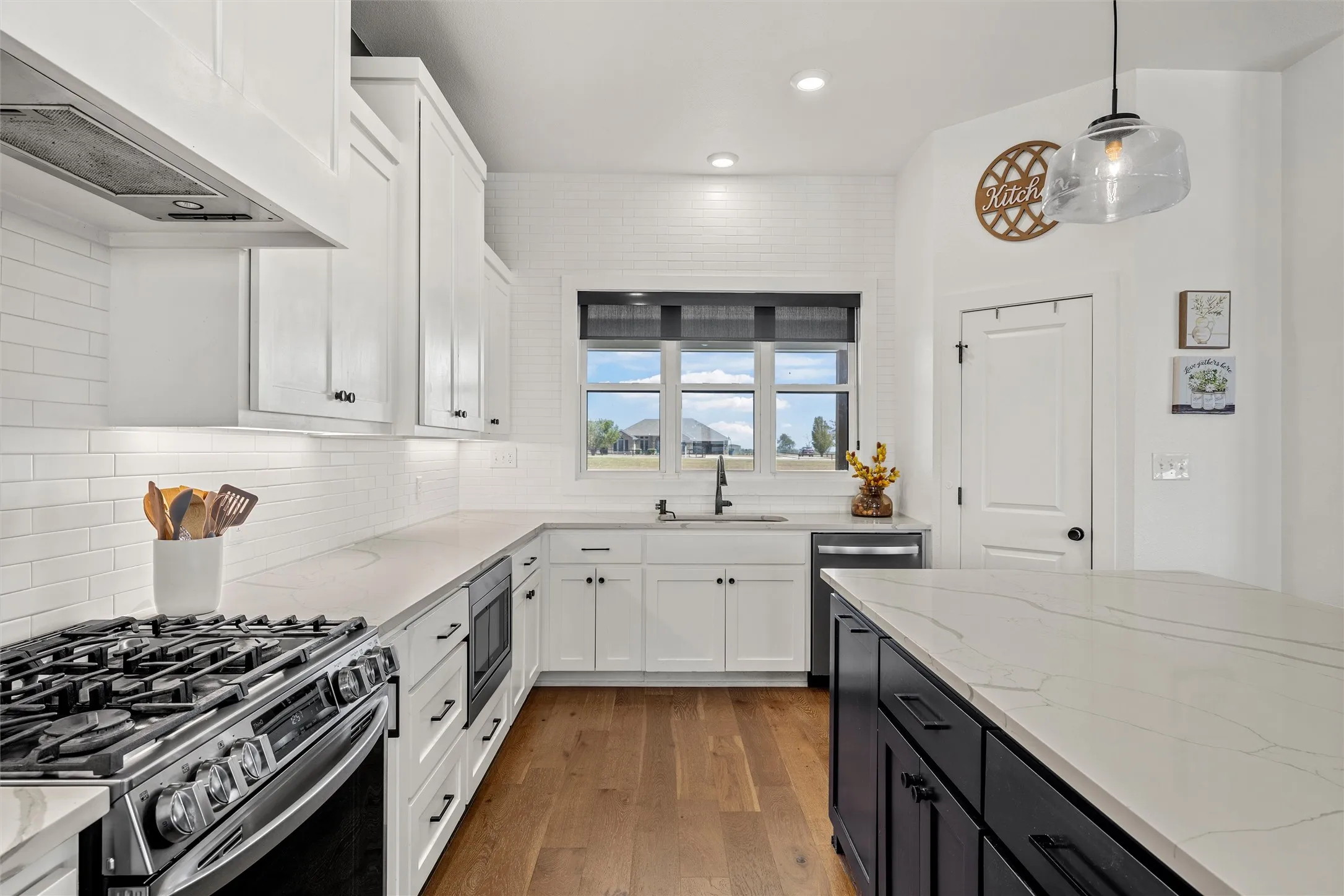 White shaker cabinetry, wood-finish flooring, stainless steel appliances, built-in microwave, and a black kitchen island