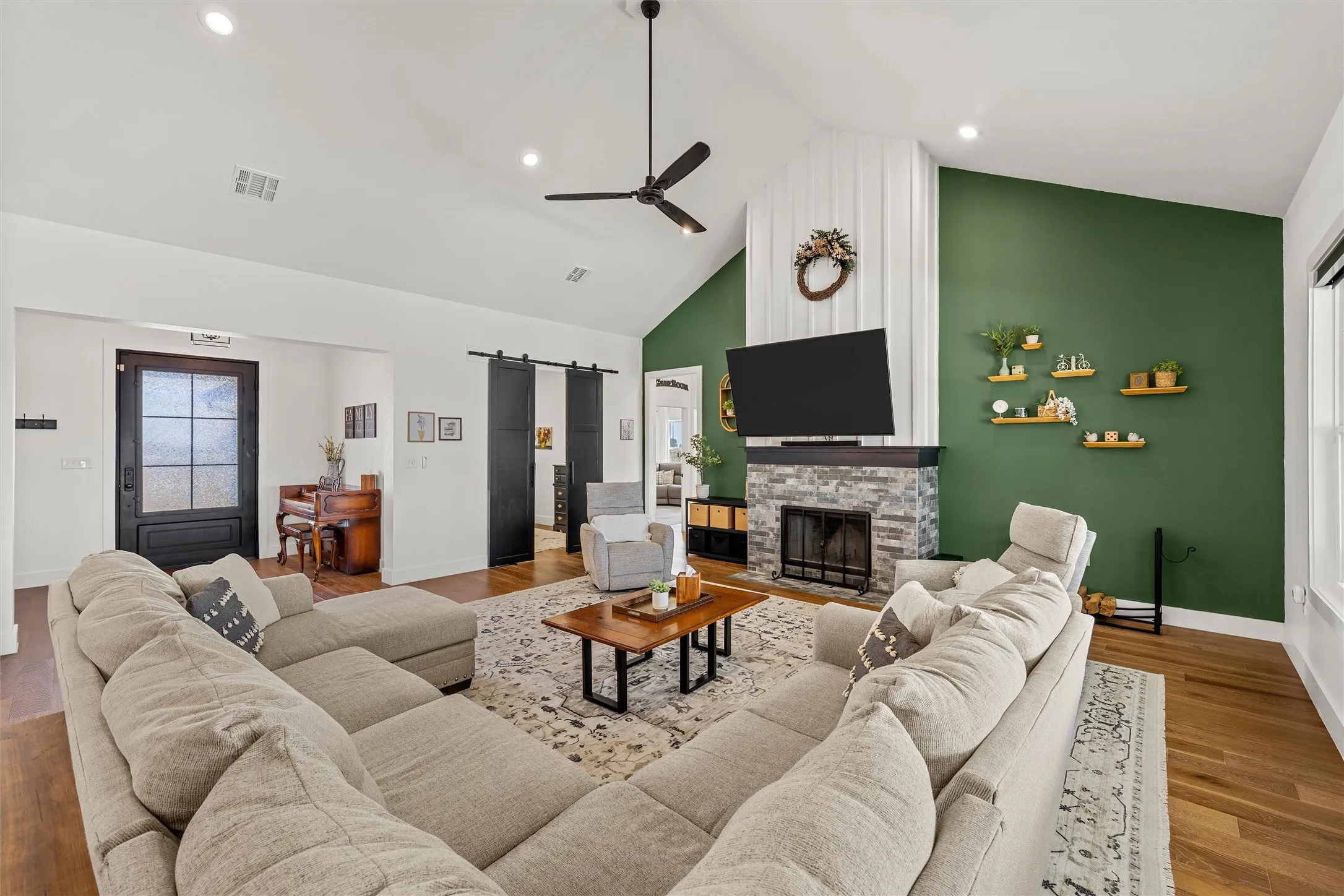 Vaulted ceilings with recessed lighting, wood-finish flooring, a stone-clad fireplace with a dark wood mantel, and built-in barn doors