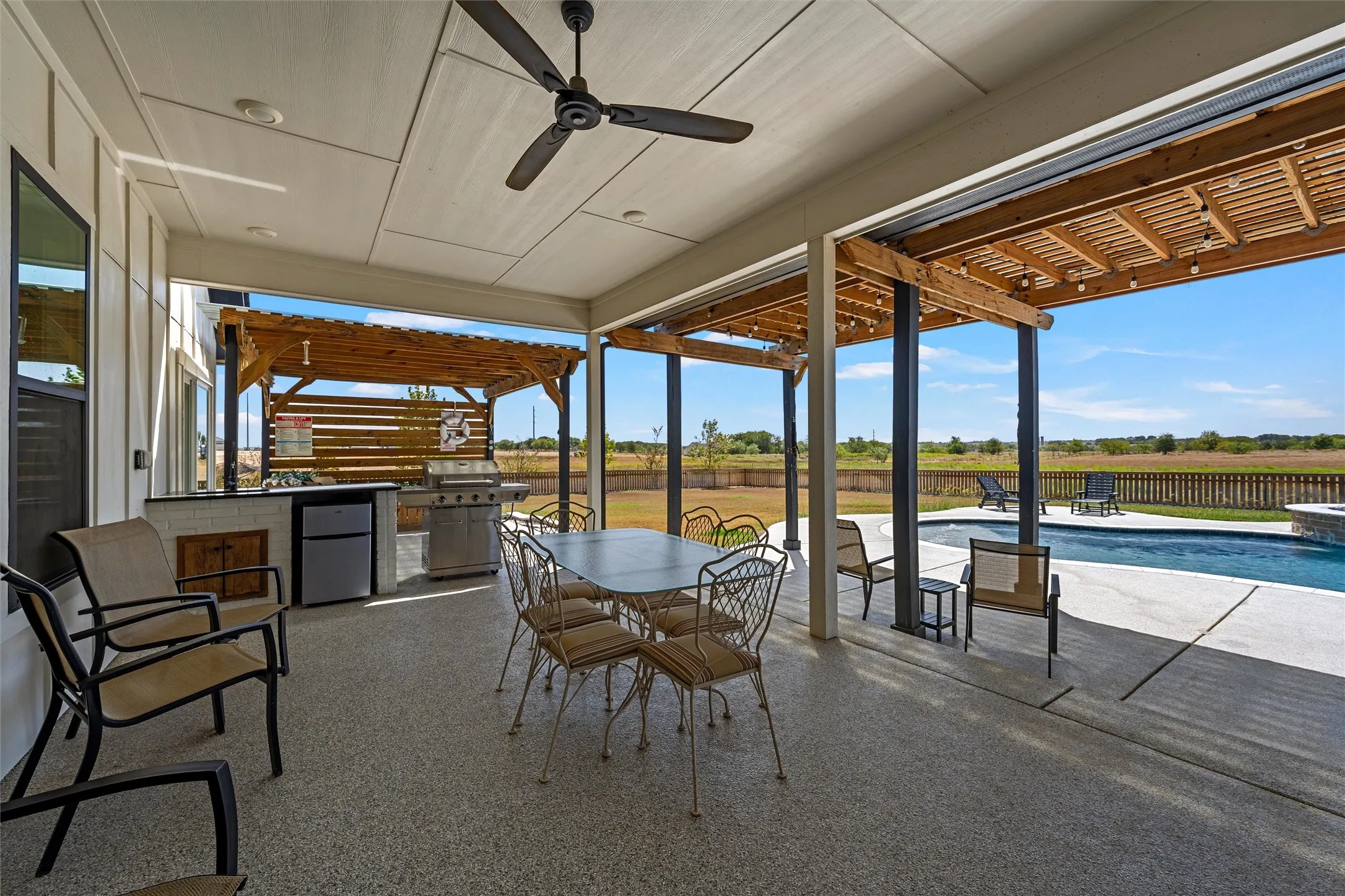 Covered patio featuring an outdoor kitchen with built-in grill, wood pergola, ceiling fan, recessed lighting, and a swimming pool