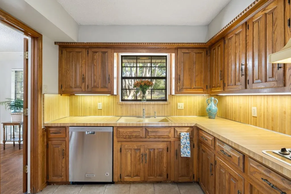 Kitchen featuring wood cabinetry, integrated stainless steel dishwasher, and a window above the sink