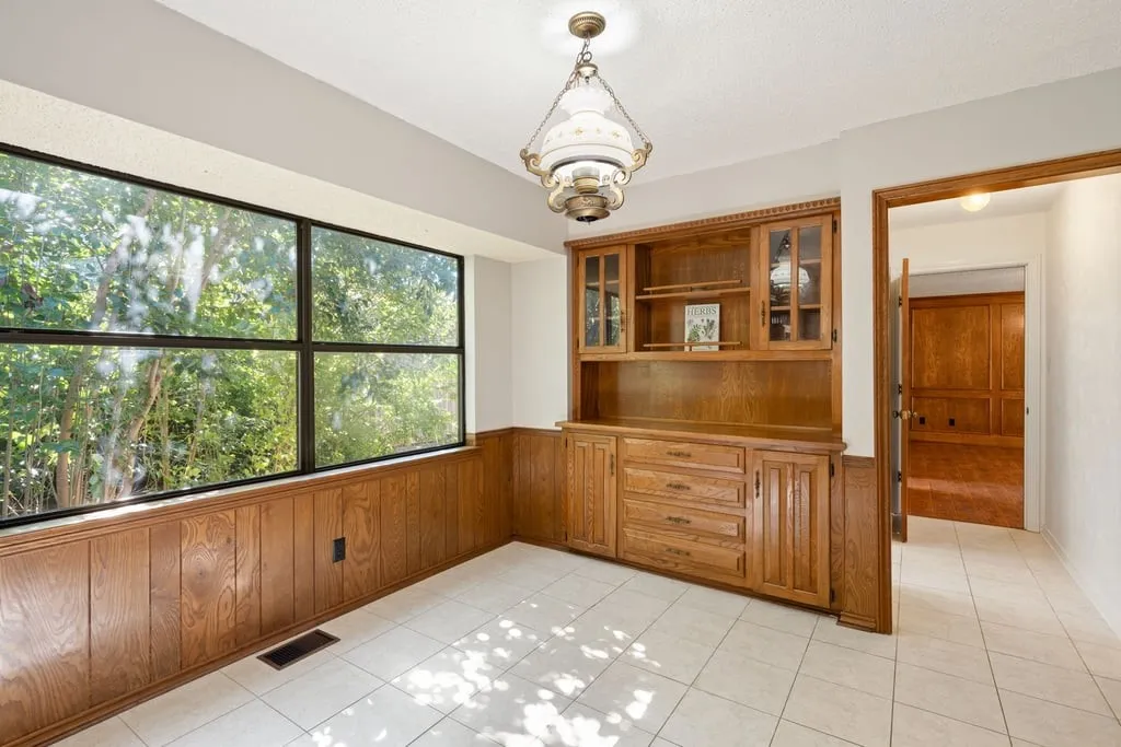 Extensive window with black framing, wood-paneled wainscoting, built-in wood cabinetry with glass door accents, and tile flooring