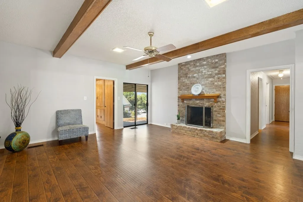 Wood-finish flooring, exposed ceiling beams, brick-clad fireplace with mantel, and sliding glass doors
