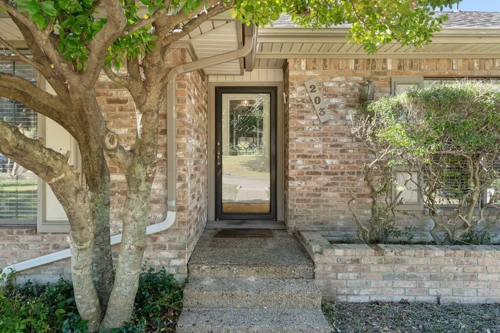 Brick facade with a full-light entry door, concrete steps, and integrated brick planter