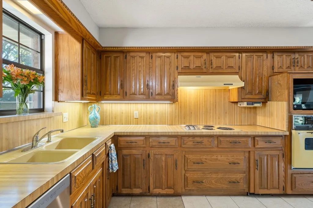 Kitchen featuring wood cabinetry, integrated appliances, double basin sink, and a window