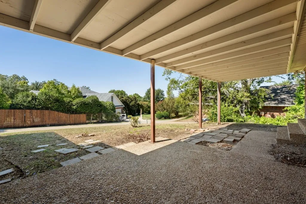 Covered patio featuring an exposed aggregate concrete surface, concrete steps, and a wooden fence