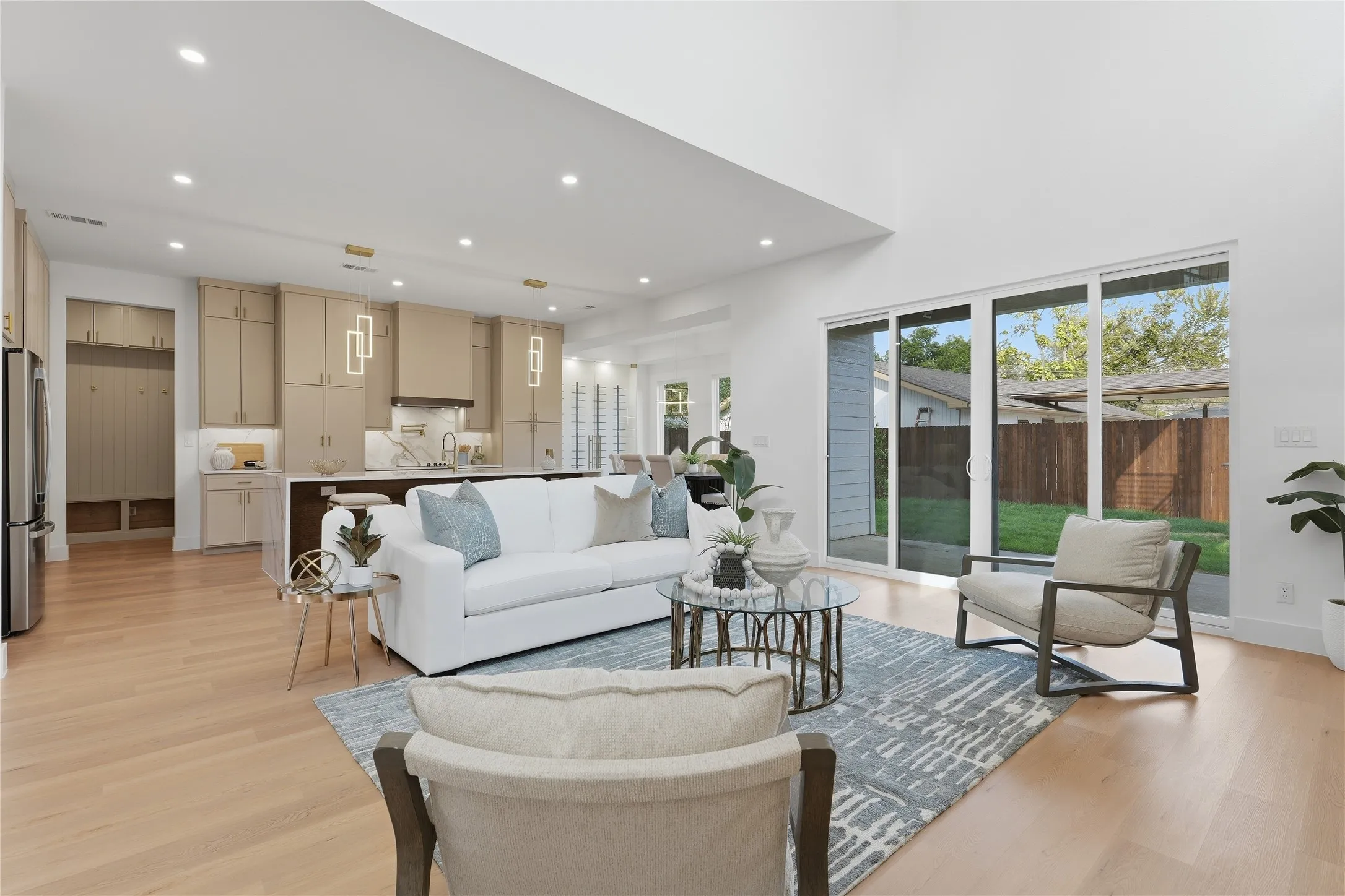 Vaulted ceiling with recessed lighting, light wood-finish flooring, full wall of sliding glass doors, white shaker cabinetry with gold hardware, and stainless steel appliances
