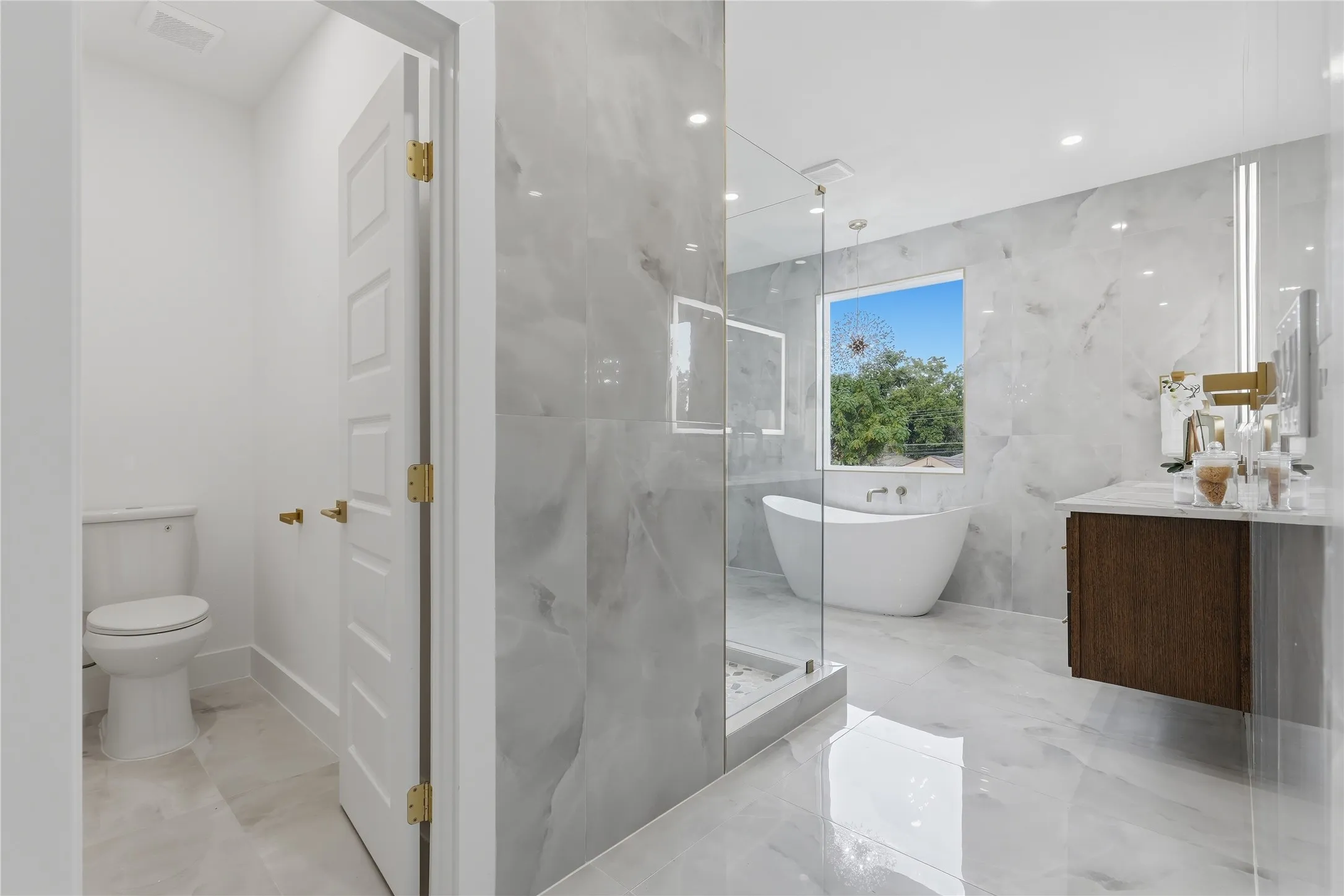 Floating vanity with a light-colored countertop, freestanding soaking tub, large window, and wall-mounted plumbing fixtures