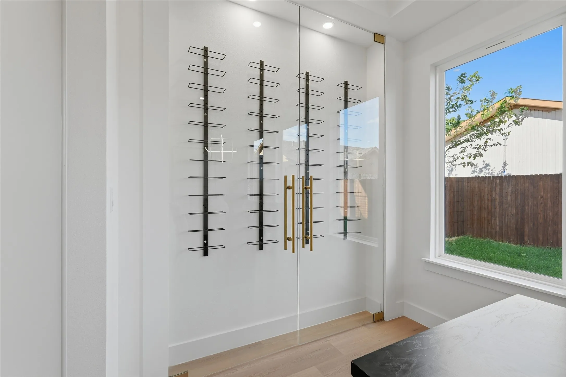 Glass-enclosed storage with black metal shelving, brass-finish hardware, and recessed overhead lighting