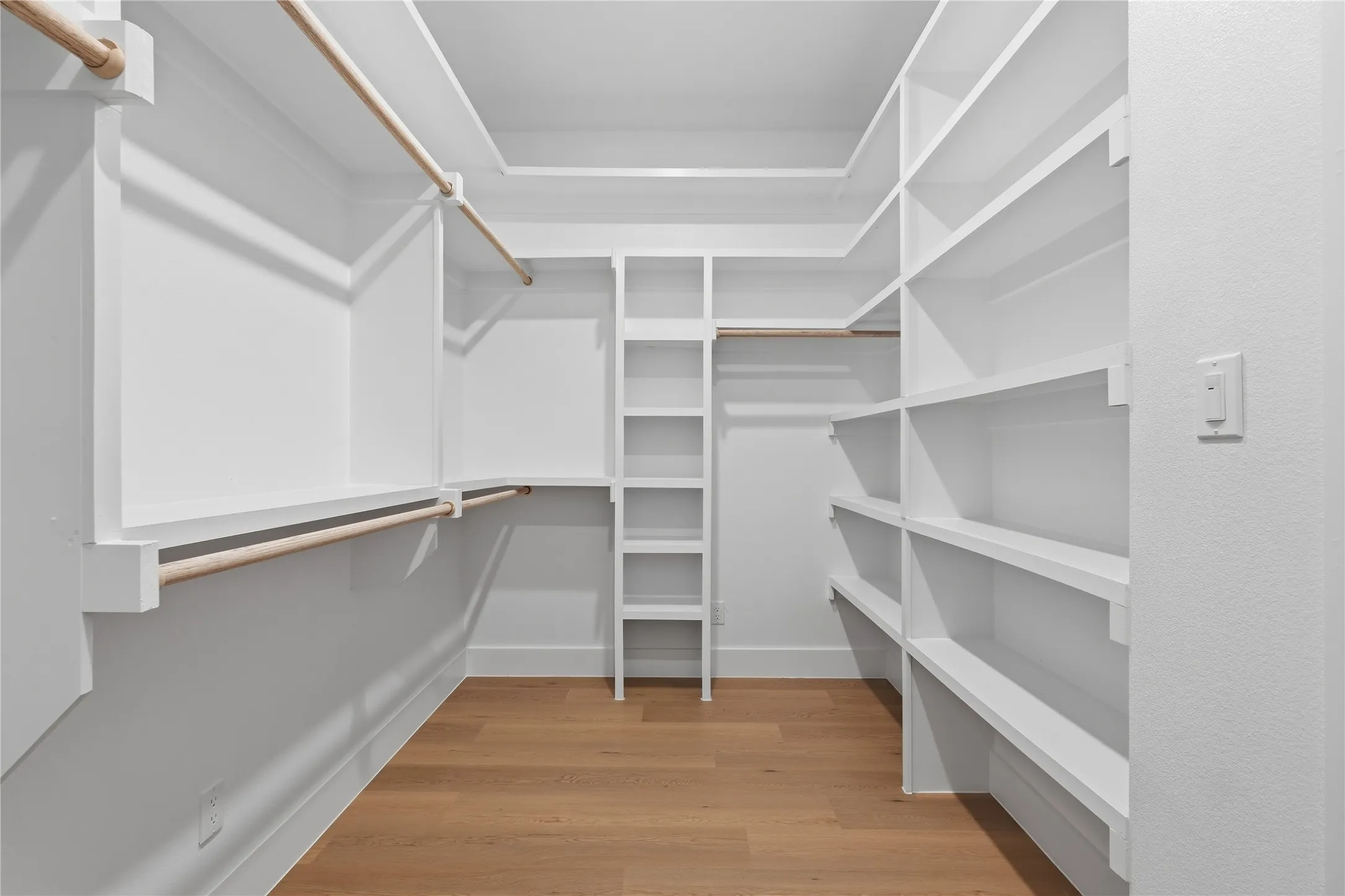 Walk-in closet featuring built-in white shelving, multiple hanging rods, and wood-finish flooring