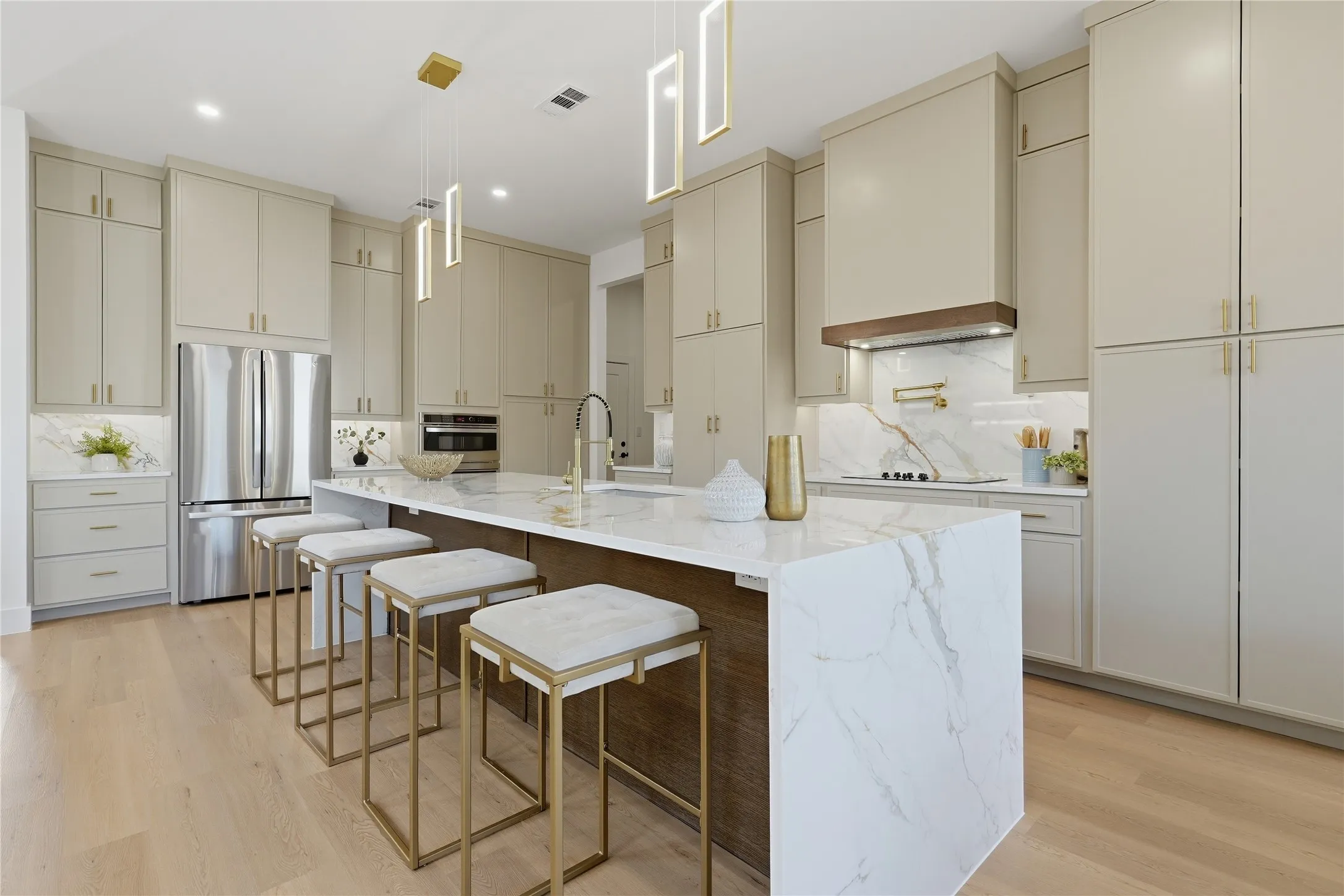 Kitchen featuring light wood-finish flooring, a waterfall island with stone countertop, stainless steel appliances, pendant lighting, and abundant cabinetry