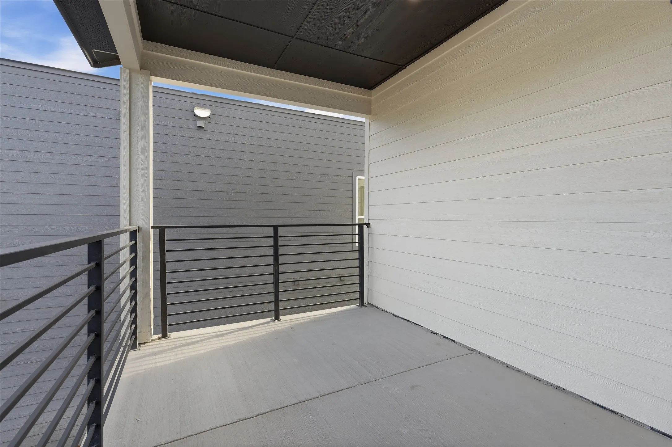 Covered balcony with concrete flooring, modern black horizontal railing, and light-toned siding
