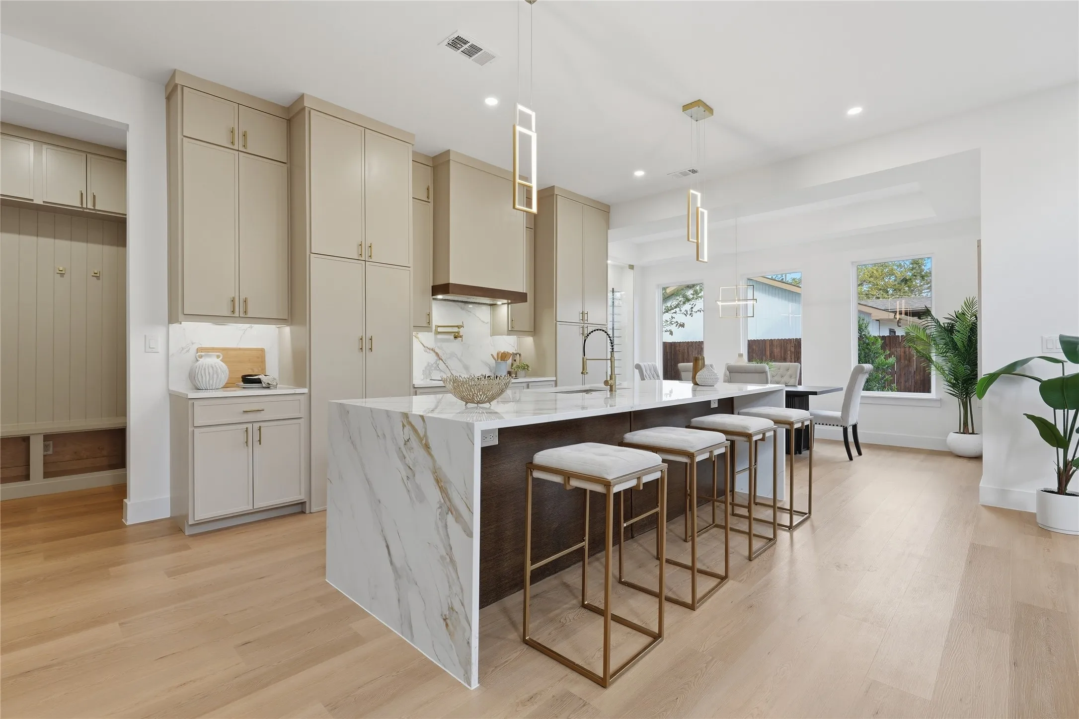 Expansive kitchen island with a waterfall countertop, light-toned cabinetry, wood-finish flooring, and contemporary pendant lighting