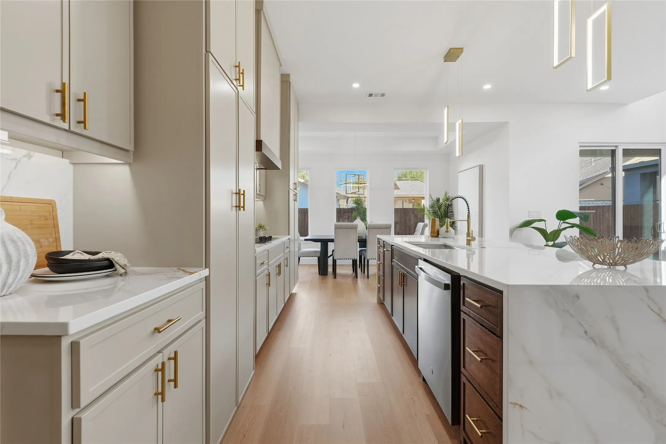 Gourmet kitchen featuring a large waterfall island with integrated sink, two-tone cabinetry, wood-finish flooring, and contemporary pendant lighting