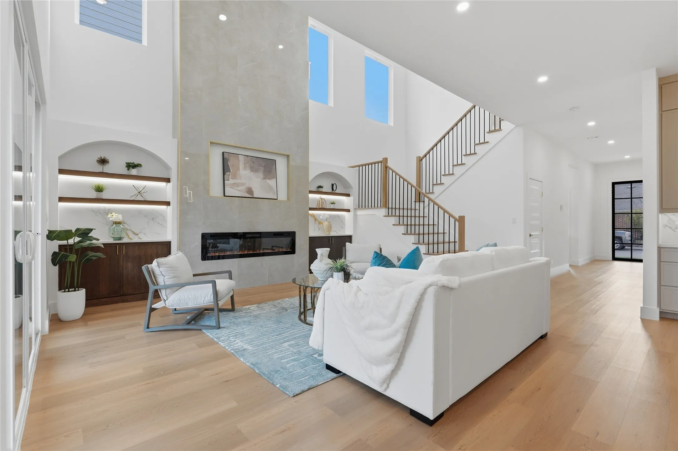 Two-story living area with wood-finish flooring, a linear fireplace set in a stone-look accent wall, and built-in shelving with integrated lighting