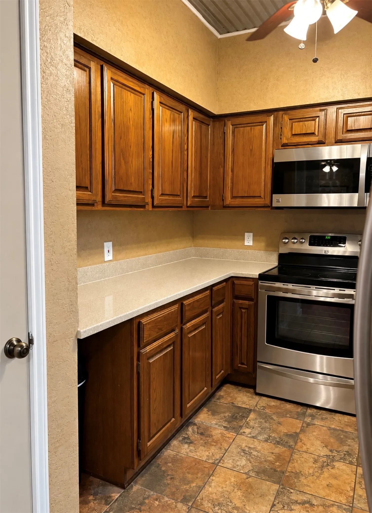 Wood-finish cabinetry paired with light countertops, stainless steel appliances, and a tiled floor