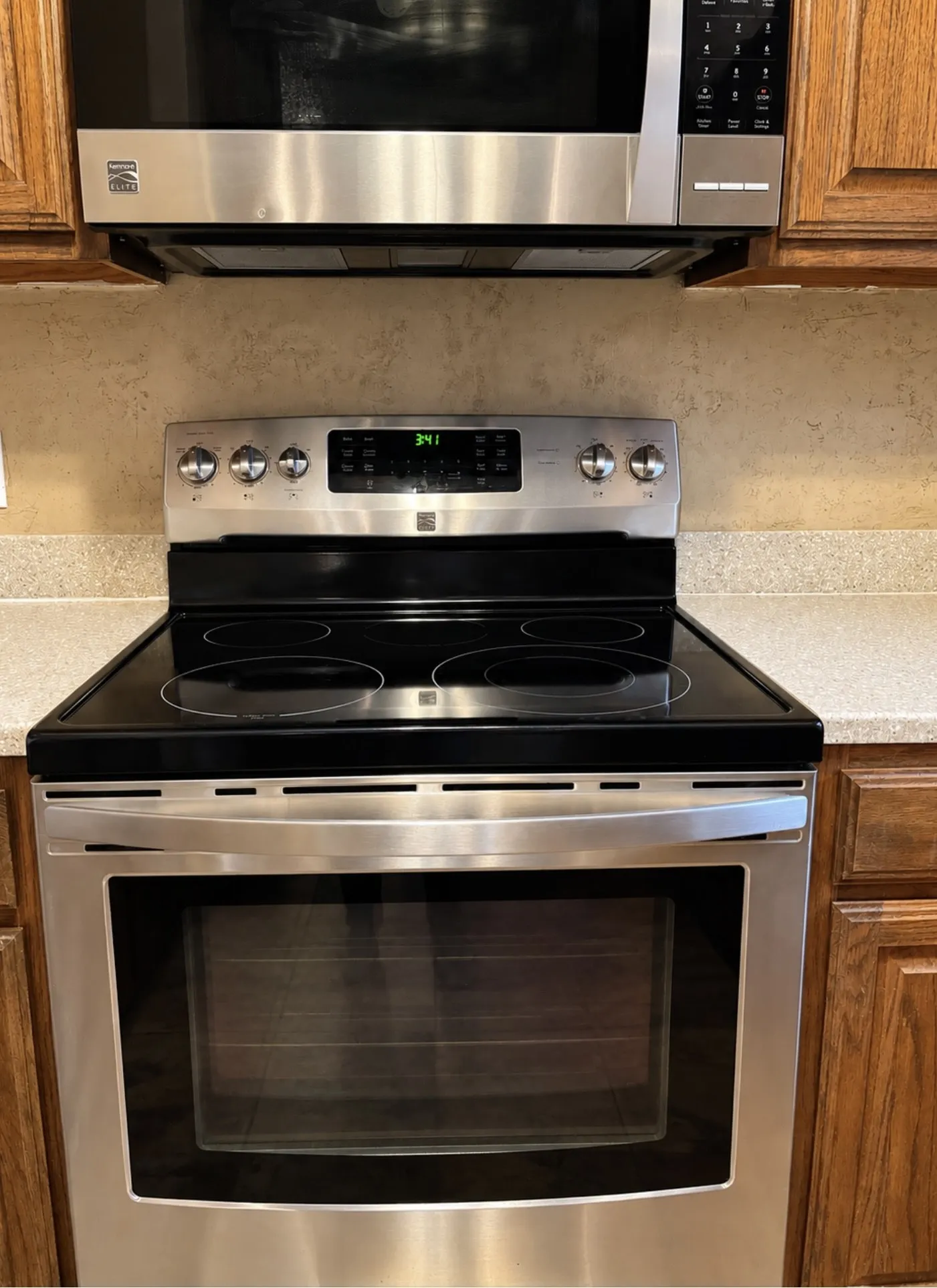 Stainless steel electric range with a smooth cooktop, coordinating microwave, and wood-finish cabinetry
