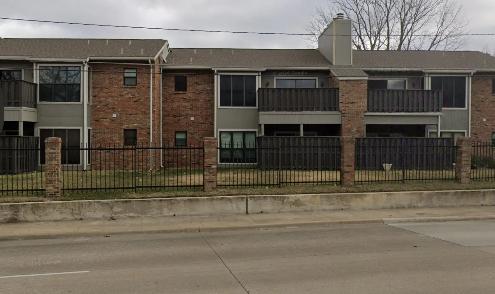 Brick and siding exterior with multiple balconies, a chimney feature, and a wrought iron fence with brick pillars