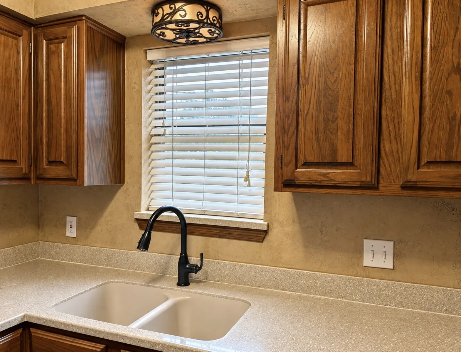 Wood-finish cabinetry, dual basin sink, integrated countertop, and matte black gooseneck faucet