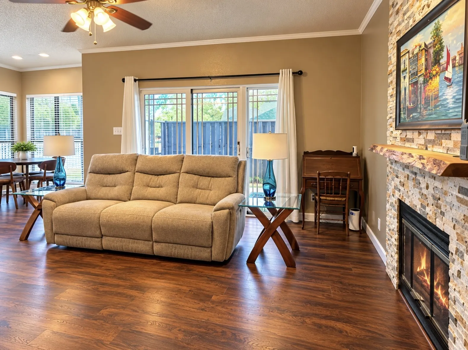 Wood-finish flooring throughout, a stone-clad fireplace with a wood mantel, and sliding glass doors with privacy blinds