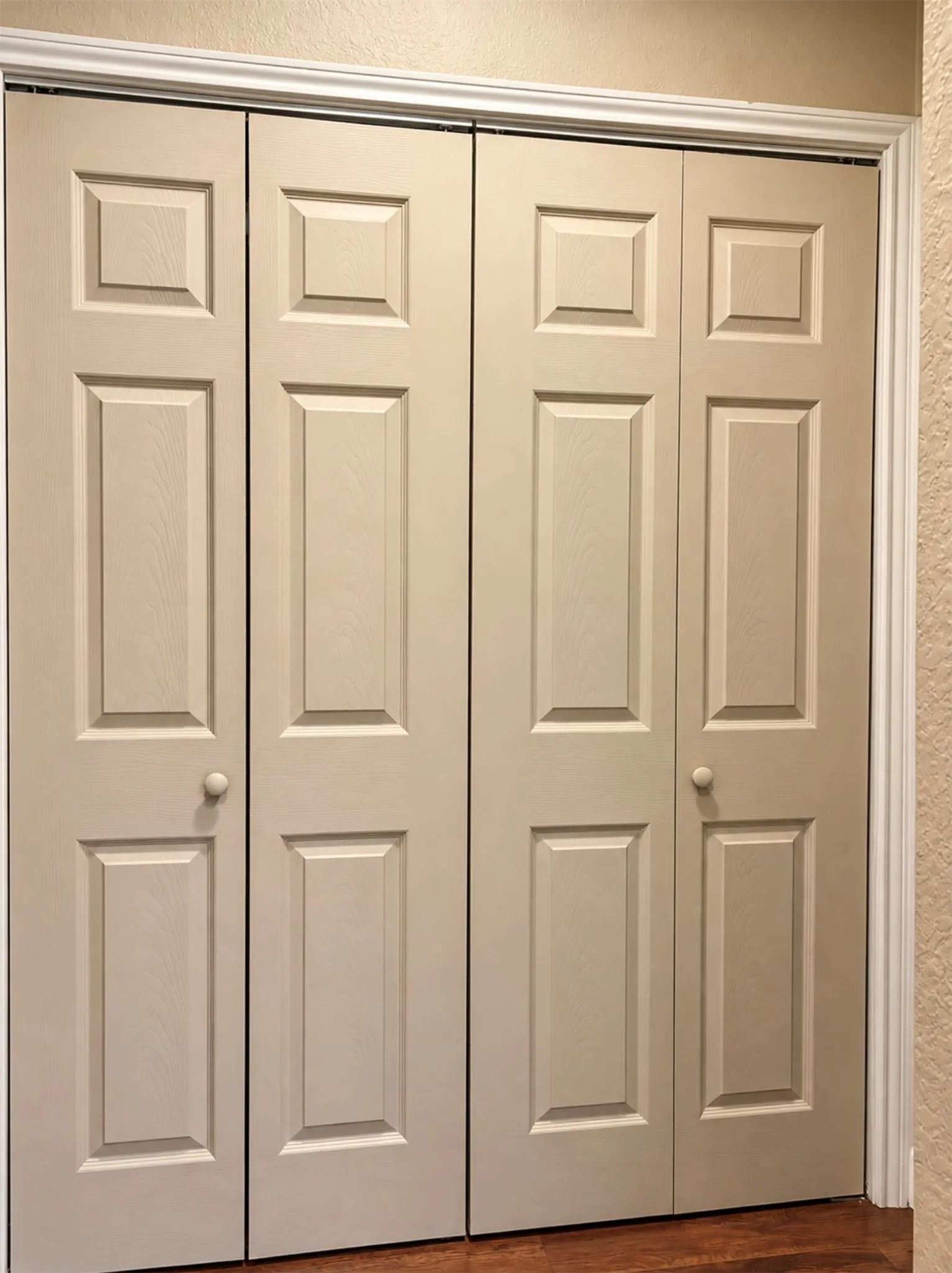 Bi-fold doors with panel detailing, white trim, and wood-finish flooring