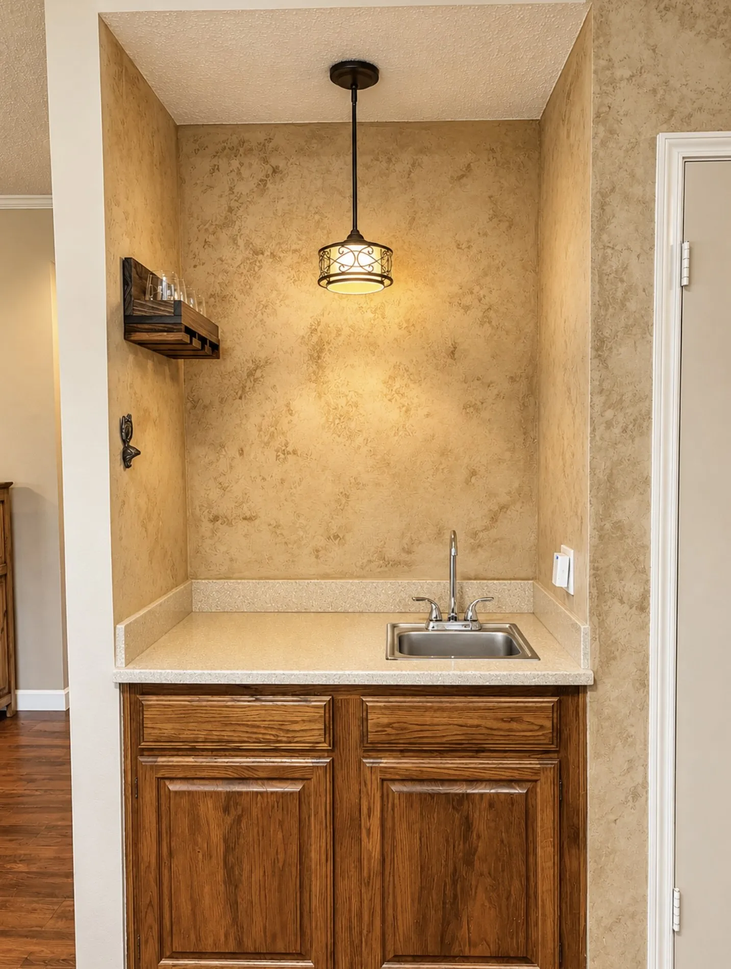 Built-in wet bar featuring a stainless steel sink, chrome faucet, light-toned countertop, and rich wood-finish cabinetry