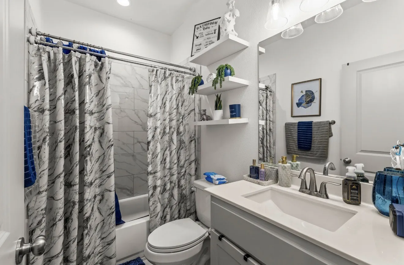 Shower-tub combination with tile surround, single-sink vanity with countertop, wall-mounted mirror, and floating shelving