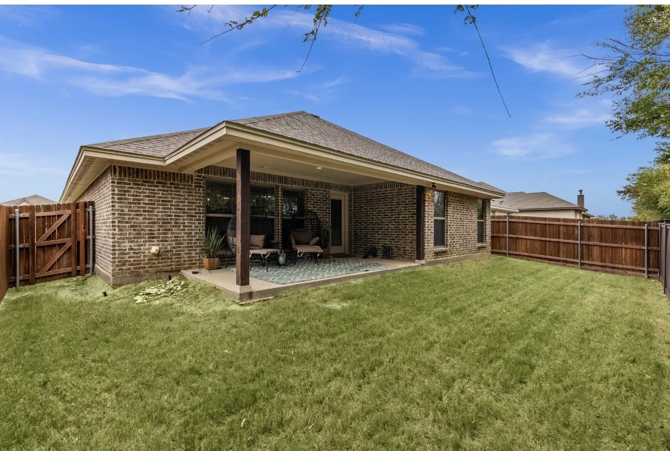Brick exterior with a covered patio, solid wood privacy fencing, and a grassy lawn