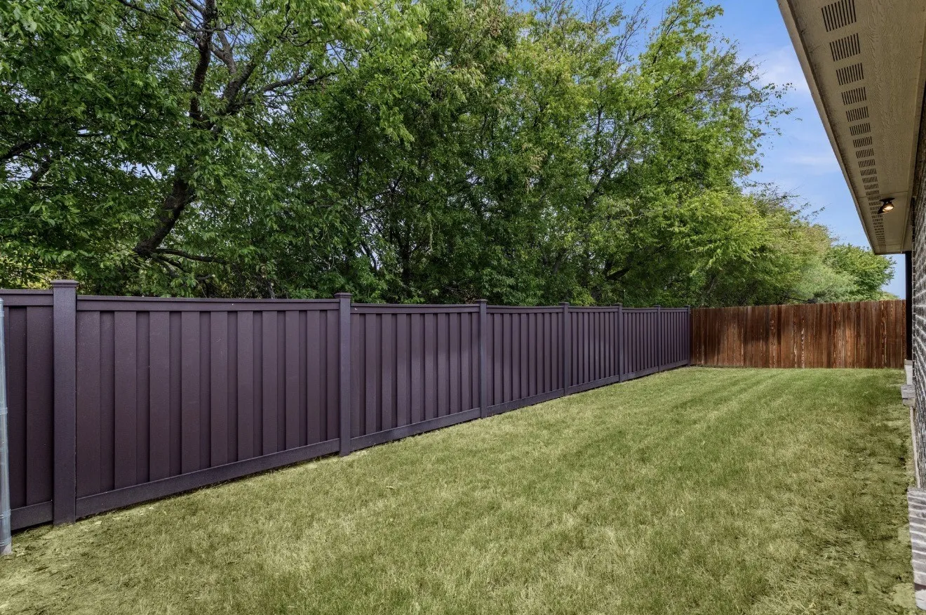Spacious lawn featuring a brown privacy fence, a wooden fence, and mature trees