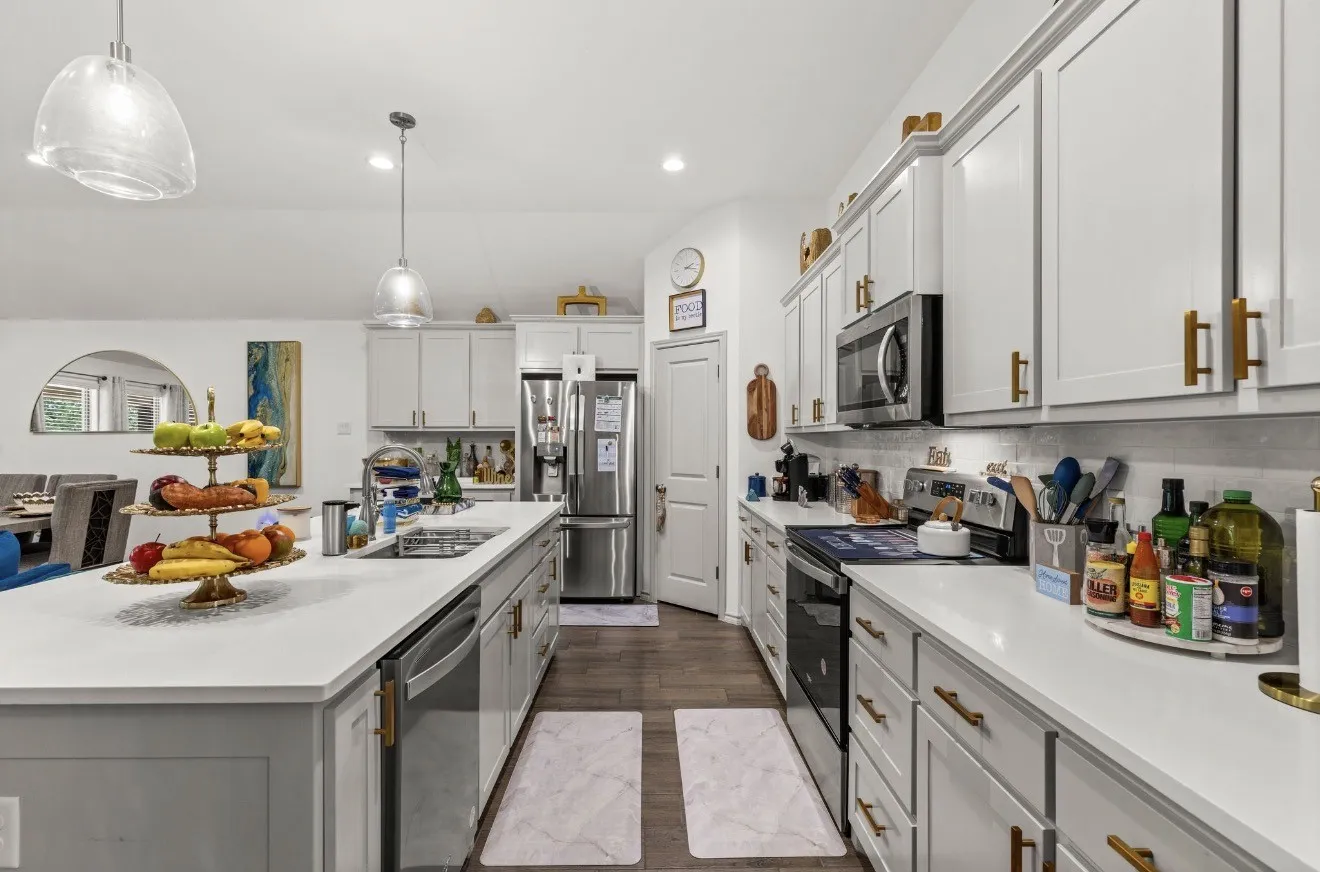 White cabinetry with gold-tone hardware, stainless steel appliances, light-toned countertops, and wood-finish flooring