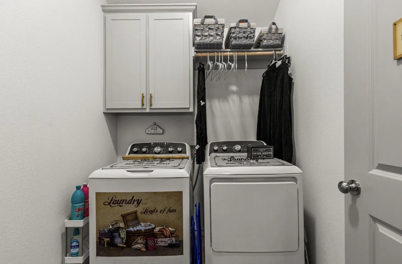 Integrated laundry area with white appliances, overhead cabinetry, and built-in clothes rod