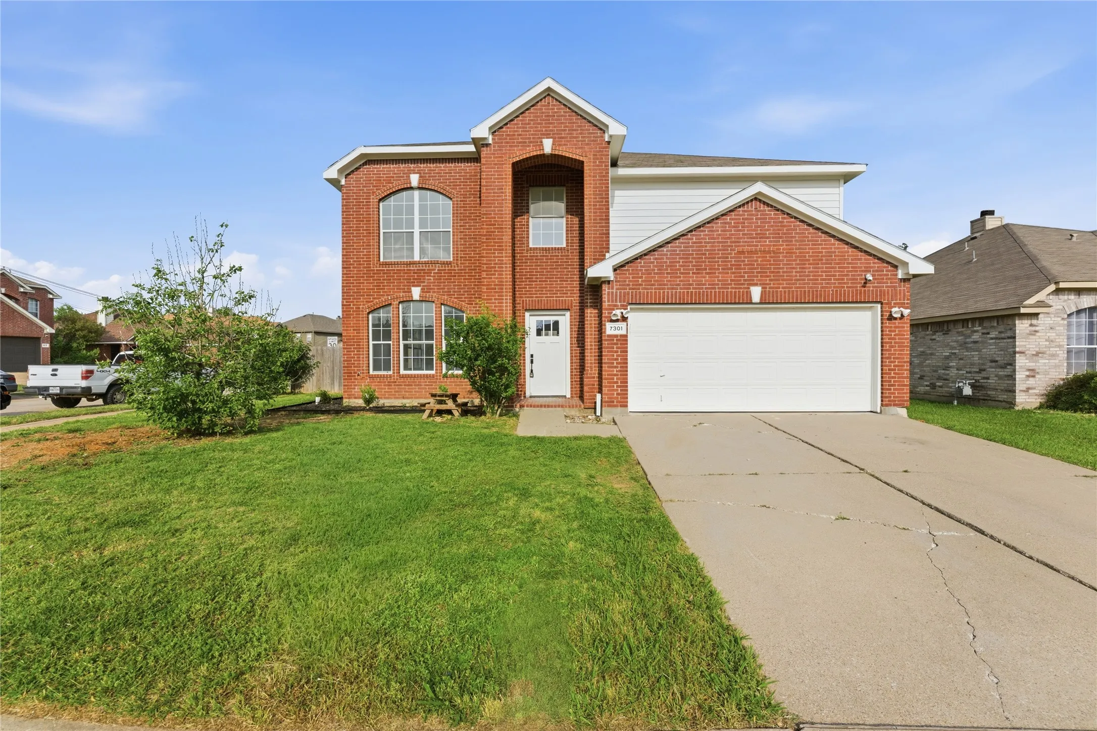 Brick facade residence featuring an integrated two-car garage, arched window accents, and a prominent front entry