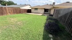 Expansive fenced backyard featuring a concrete patio, brick exterior, and mature landscaping