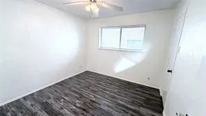 Wood-finish flooring, white walls, and a ceiling fan with integrated lighting