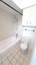 White tile flooring, white bathtub with shower, white wall-mounted cabinetry, and a white toilet