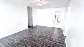 Wood-finish flooring, white walls, ceiling fan with light fixture, and a glass-paneled door