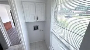 White cabinetry with dark hardware, a window with horizontal blinds, and square floor tiles