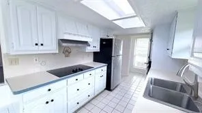 White cabinetry with dark hardware, dual-basin stainless steel sink, integrated cooktop, stainless steel refrigerator, and tiled flooring