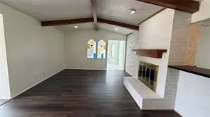 Vaulted ceiling with exposed wood beams, wood-finish flooring, white painted brick fireplace with hearth, and a wood mantel