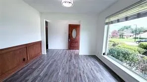 Wood-finish flooring, wood paneling, front entry door with oval glass insert, large picture window, and ceiling-mounted light fixture