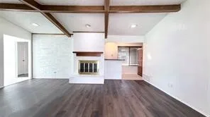 Vaulted ceiling with exposed wood beams, wood-finish flooring, white brick-accent wall, and a white brick fireplace with a wood mantle