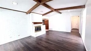 Vaulted ceiling with exposed wood beams, wood-finish flooring, white brick-finish fireplace, and white painted walls