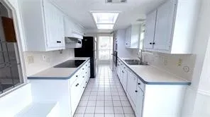 Galley kitchen featuring white cabinetry, light countertops, an integrated cooktop, a skylight, and tiled flooring