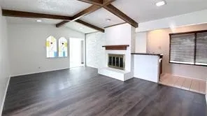 Vaulted ceiling with exposed wood beams, wood-finish flooring, fireplace with a white hearth and wood mantel, and stained glass window accents