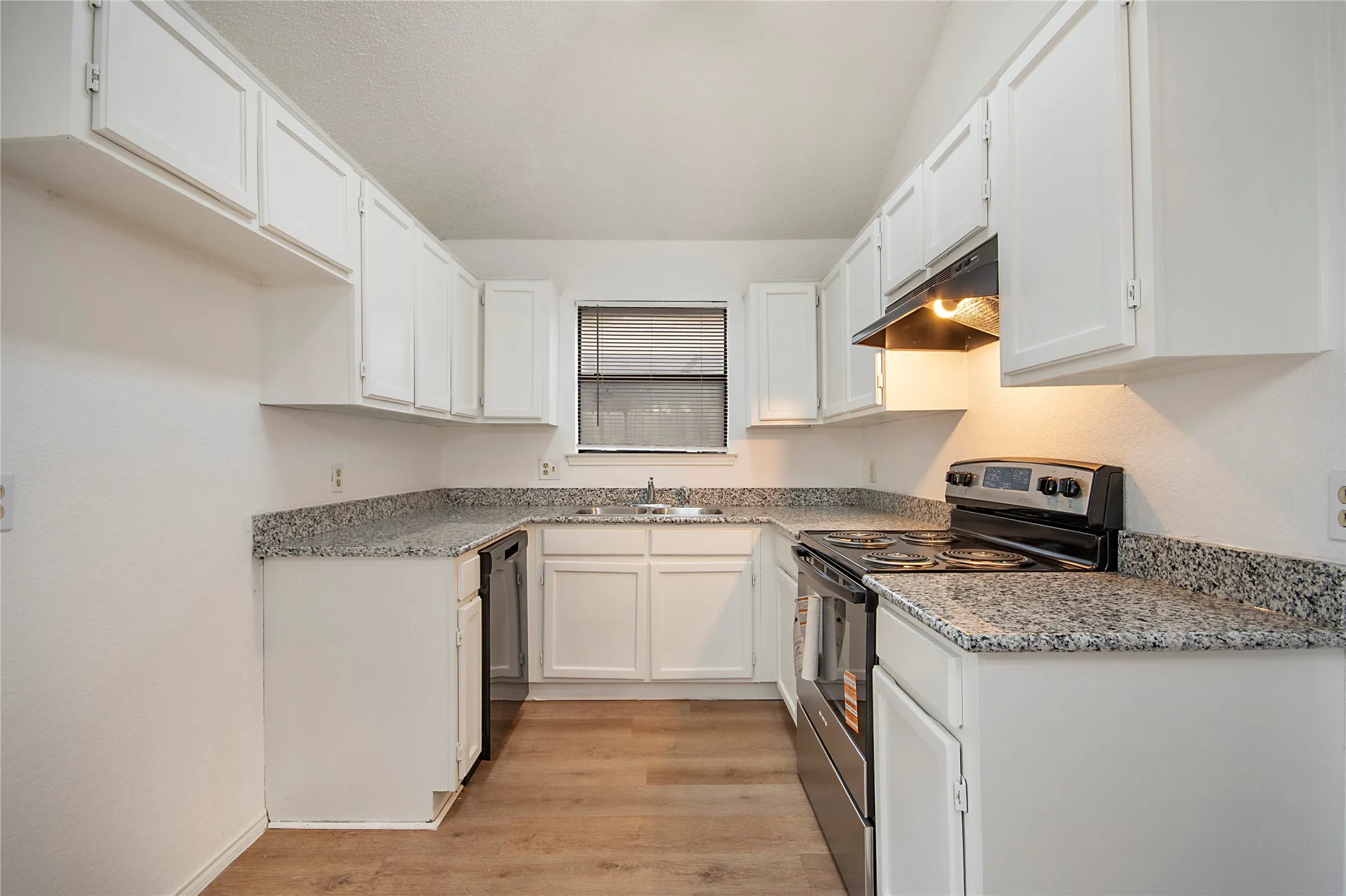 U-shaped kitchen featuring white cabinetry, light-toned countertops, wood-finish flooring, a stainless steel electric range, and a window with blinds
