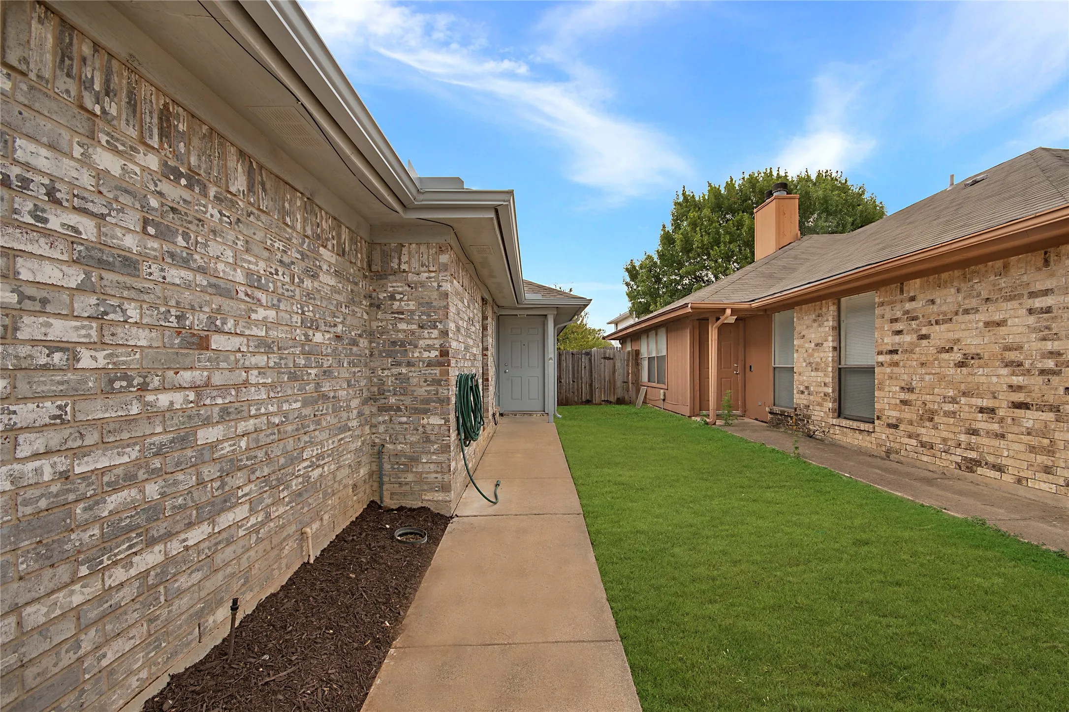 Brick exterior with a concrete walkway, mature landscaping, and an adjacent green space