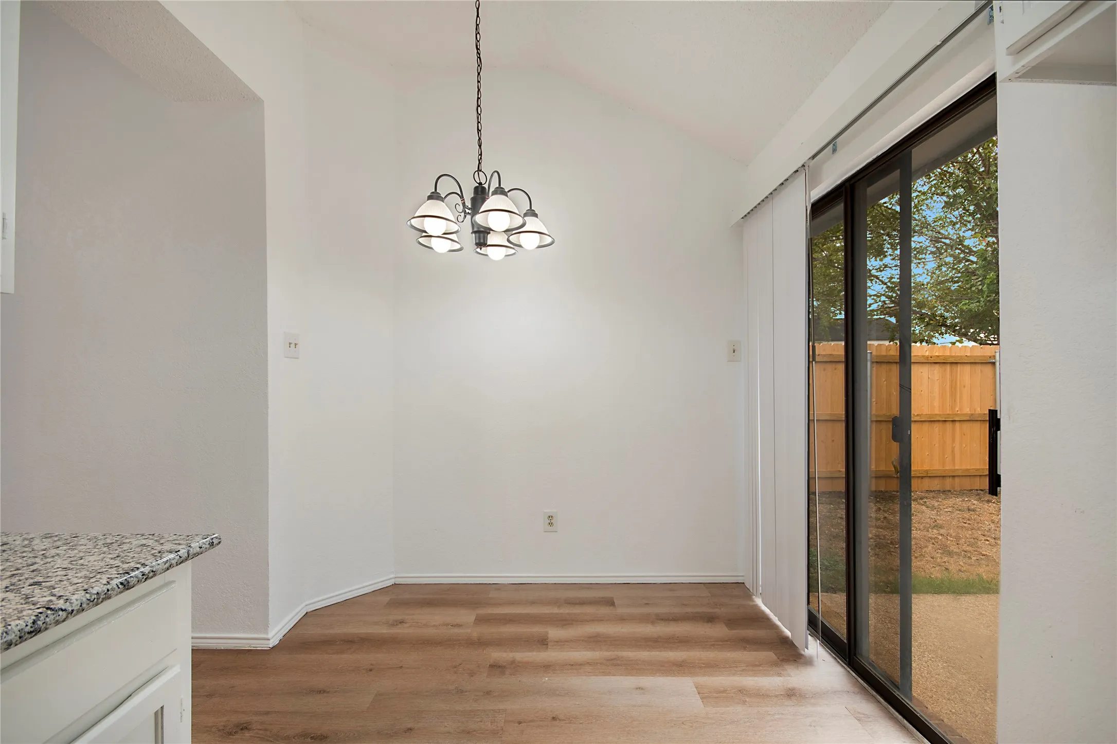 Vaulted ceiling, wood-finish flooring, sliding glass door, overhead chandelier, white cabinetry with granite-style countertop